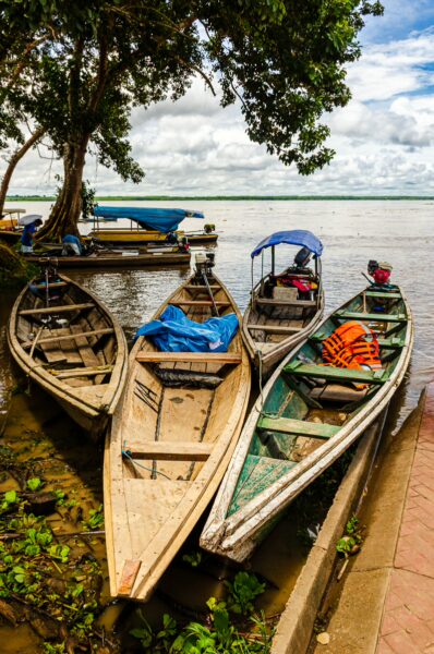 Rustic boats lined along the riverbank with lush greenery, reflecting the vibrant life in Puerto Nariño, Amazonas, Colombia.