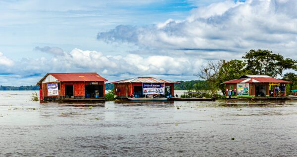 Colorful wooden houses reflect on the flooded waters of Puerto Narino, Amazonas, Colombia, under a cloudy sky.