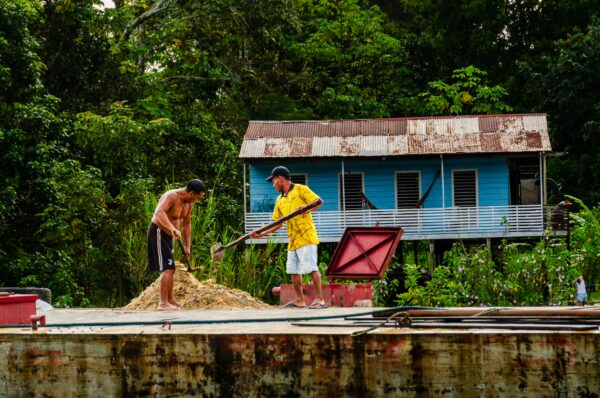 Men working with tools near a vibrant blue house surrounded by lush greenery in Leticia, Amazonas, Colombia.