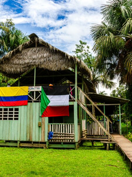 Colorful flags of Colombia, Italy, and Germany adorn a thatched-roof structure in lush Puerto Nariño, Amazonas, Colombia.