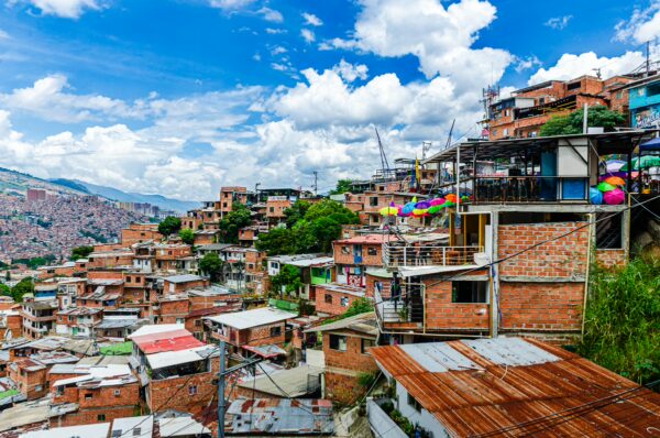 Colorful houses cascade down the hillside of Comuna 13 in Medellín, Colombia, under a bright blue sky with fluffy clouds.