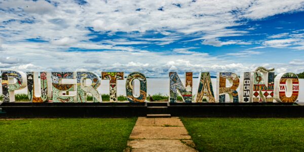 Colorful "Puerto Nariño" sign stands against a bright sky, highlighting the vibrant art and lush greenery of Amazonas, Colombia.