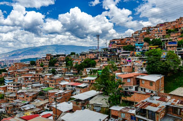 Vibrant hillside of Comuna 13 in Medellín, showcasing colorful houses against a backdrop of rolling clouds and mountains.