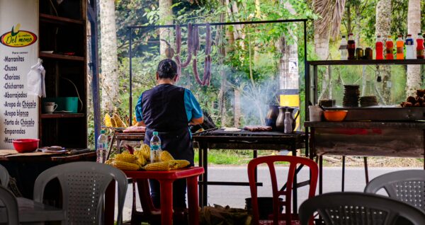 Cooking area in Salento, Quindio, Colombia, features a chef grilling, surrounded by lush greenery and colorful condiments.