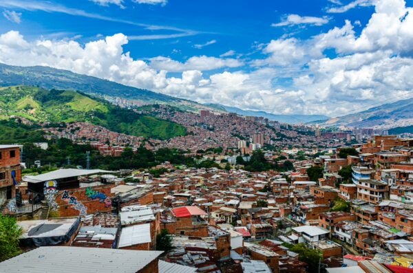Vibrant panorama of Medellín's Comuna 13, showcasing colorful buildings nestled in the hills under a blue sky with fluffy clouds.