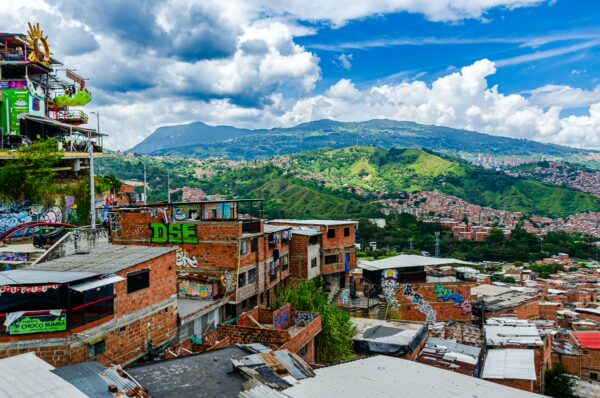 Vibrant hillside community of Comuna 13 in Medellín, showcasing colorful buildings against a backdrop of lush mountains and blue skies.