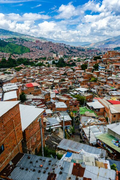 A vibrant view of Comuna 13 in Medellín, showcasing colorful rooftops and mountainous backdrop under a blue sky dotted with clouds.