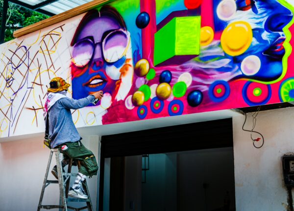 Vivid street art adorns a wall in Comuna 13, Medellín, featuring colorful abstract shapes and a muralist painting.