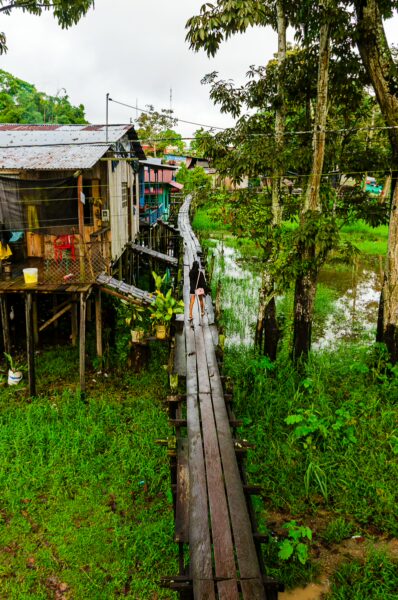 Colorful wooden houses on stilts line a narrow walkway through lush greenery near the river in Leticia, Amazonas, Colombia.