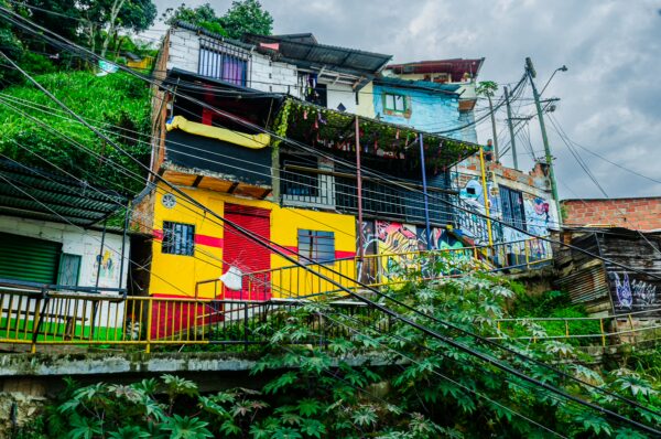 Vibrant houses in Comuna 13, Medellín, showcase colorful murals and lush greenery against a dramatic cloudy sky.