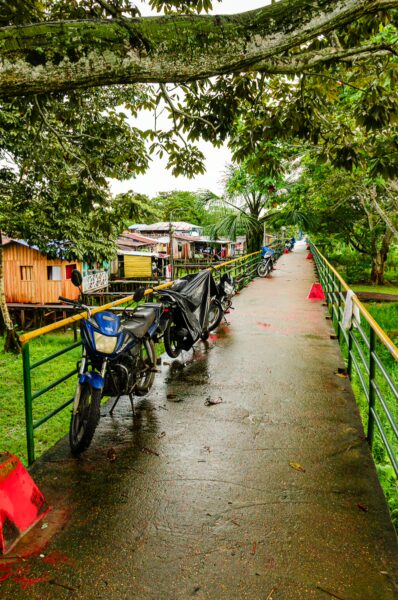 Vibrant green pathway lined with boats and wooden buildings in Leticia, Amazonas, Colombia, under a canopy of trees.