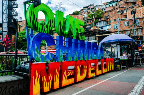 Colorful "Chimba Medellín" sign displayed in Comuna 13, surrounded by vibrant street art and steep hillside buildings.