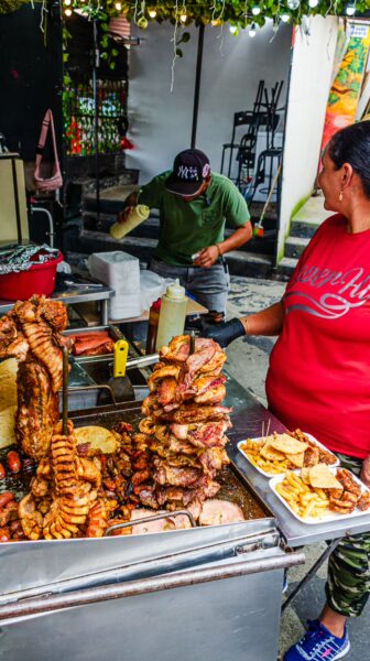 Vibrant street food scene in Comuna 13, Medellín, showcasing stacked grilled meats and a vendor preparing dishes.