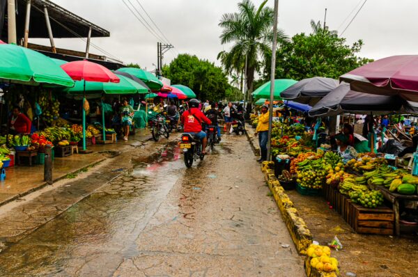 Lively market scene in Leticia, Amazonas, Colombia, featuring colorful umbrellas, fresh produce, and bustling vendors along a wet street.
