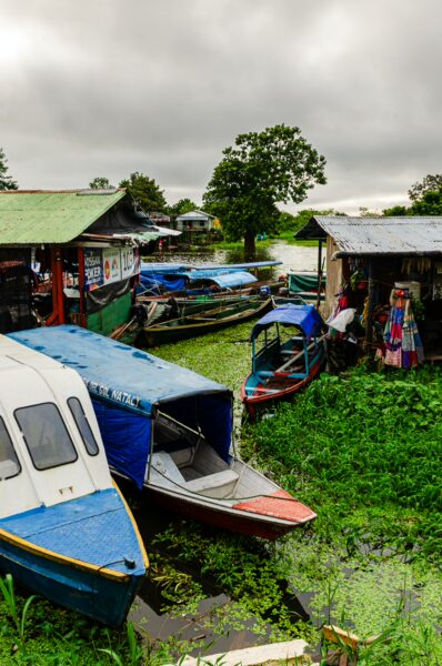 Colorful boats are moored among lush greenery in Leticia, Amazonas, Colombia, under a cloudy sky, showcasing local river life.