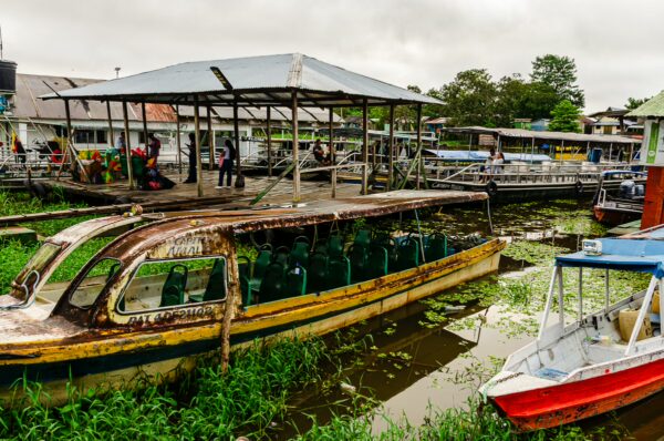 Rusting boats anchored amidst lush greenery and calm waters in Leticia, Amazonas, Colombia, under an overcast sky.