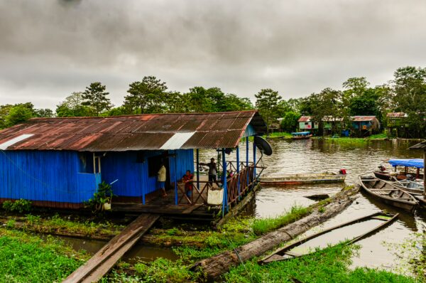 Colorful blue house by the water in Leticia, Amazonas, Colombia, surrounded by lush greenery and small boats moored nearby.