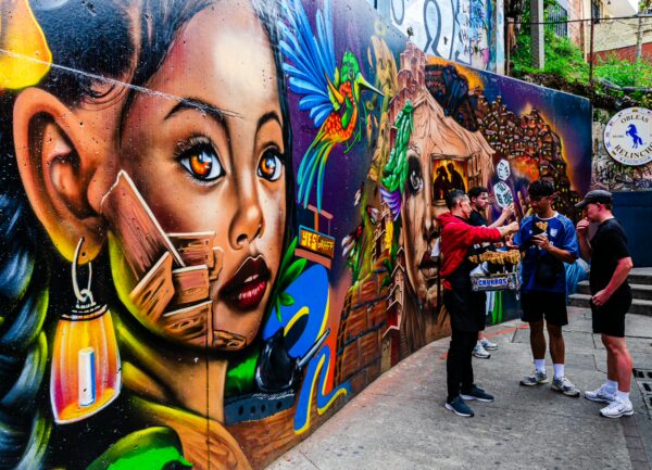 Vivid street art featuring a girl's face adorns the walls of Comuna 13, while visitors engage in lively conversation.