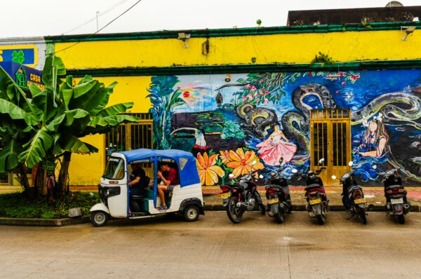 Colorful mural and vibrant yellow walls frame a busy street scene with motorcycles parked alongside a tuk-tuk in Leticia, Amazonas, Colombia.