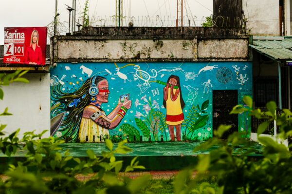 Vibrant mural depicting an indigenous figure with headphones and another character surrounded by greenery in Parque Santander, Leticia, Amazonas, Colombia.