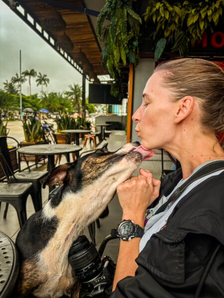 A woman shares a playful kiss with a dog at a café in Leticia, Amazonas, Colombia, surrounded by lush greenery.