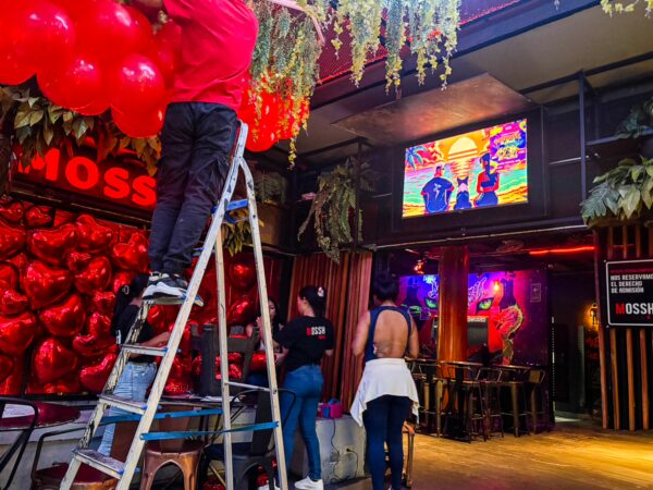 Vibrant interior of Mossh Bar in Leticia, Amazonas, Colombia, with red decor, staff arranging balloons, and colorful lighting.