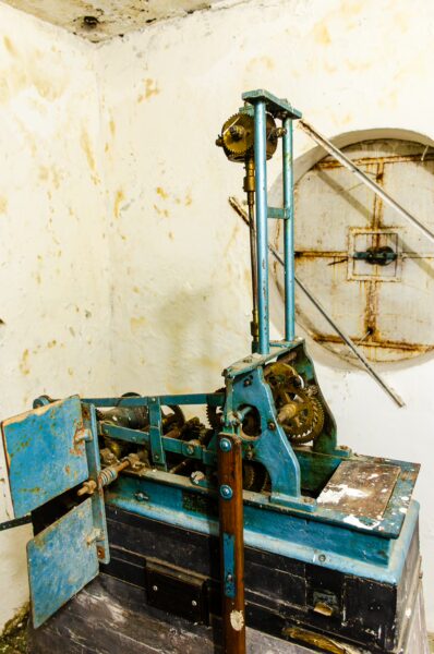 Vintage clock mechanism with intricate gears and blue accents, set against a peeling white wall in Leticia, Amazonas, Colombia.