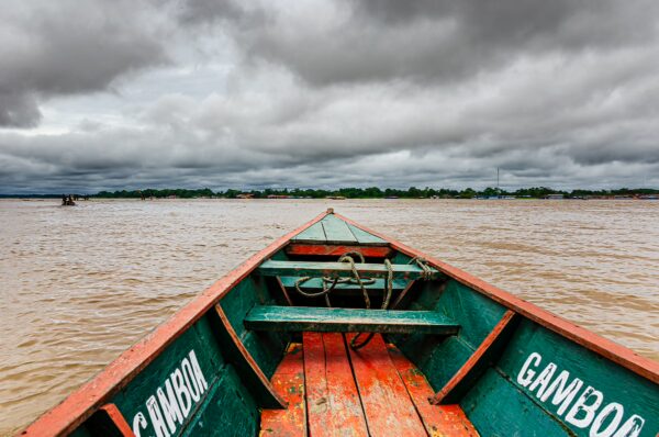 Gamboa boat bow navigating the brown waters of Leticia, Amazonas, Colombia under a moody, overcast sky.