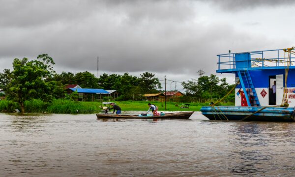 Boats navigate the brown waters of Leticia, Amazonas, Colombia, surrounded by lush greenery and cloudy skies.