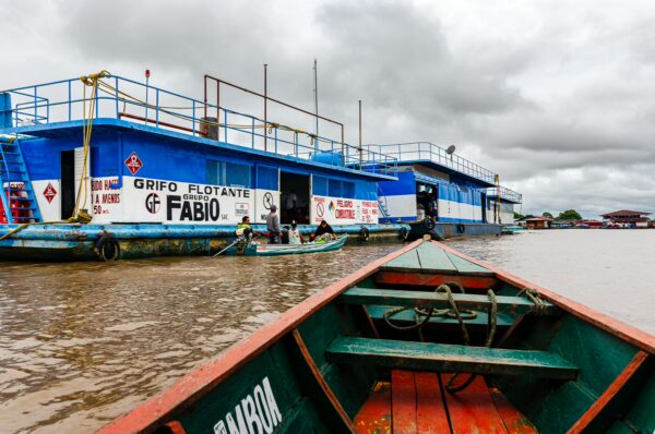Floating gas station in Leticia, Amazonas, Colombia, with a bright blue structure and boats on the Amazon River under cloudy skies.