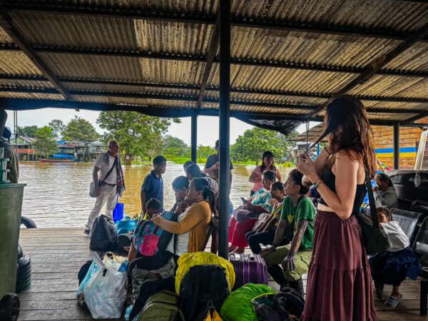 Travelers wait under a shelter by the Amazon River in Leticia, Amazonas, Colombia, surrounded by bags and backpacks.