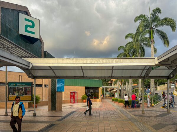 Covered bus terminal plaza in Bucaramanga with waiting passengers, palm trees, and a large platform sign