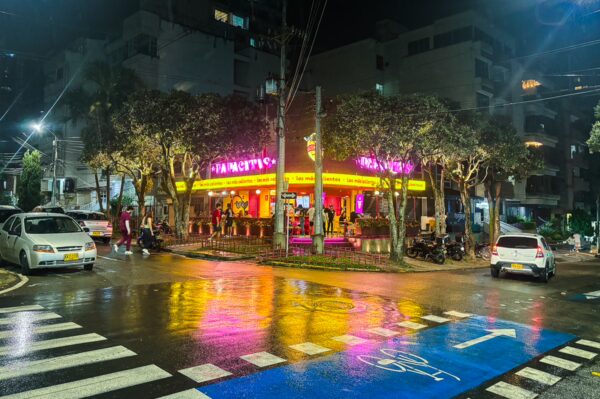Vibrant street scene in Bucaramanga, featuring a brightly lit restaurant and wet pavement reflecting colorful lights at night.