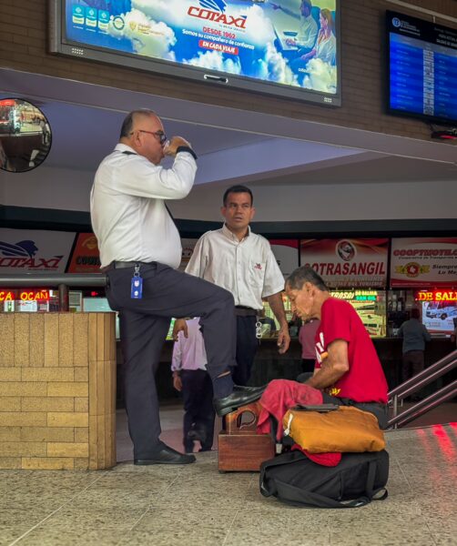 Three men in a busy transport terminal in Bucaramanga, Colombia, with a shoe shiner attending to a customer.