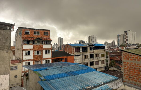 Overcast skies loom over a cityscape of Bucaramanga, revealing rooftops of colorful buildings and modern architecture in the distance.