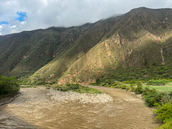 Chicamocha Canyon features lush green hills, rocky riverbanks, and a winding river flowing through the dramatic landscape.