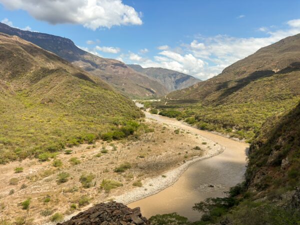 Chicamocha Canyon showcases rugged mountains, winding river, and vibrant greenery under a bright blue sky in Santander, Colombia.