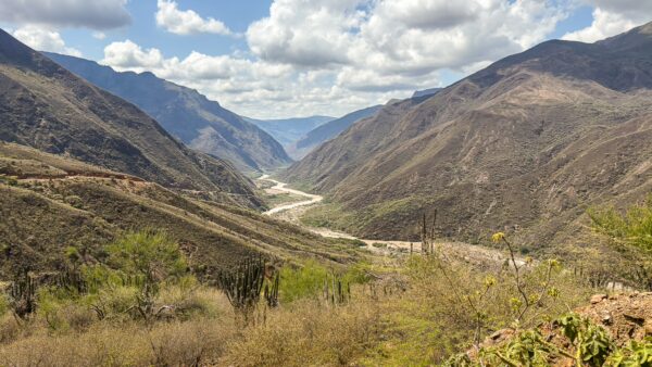 Wide view of Chicamocha Canyon in dry, rugged mountains with a river winding through the valley under a partly cloudy sky