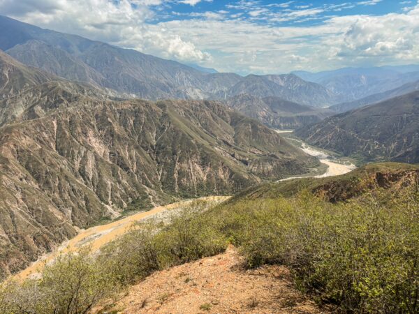 Sweeping view over Chicamocha Canyon with steep mountains, a winding river, and dry scrub in the foreground