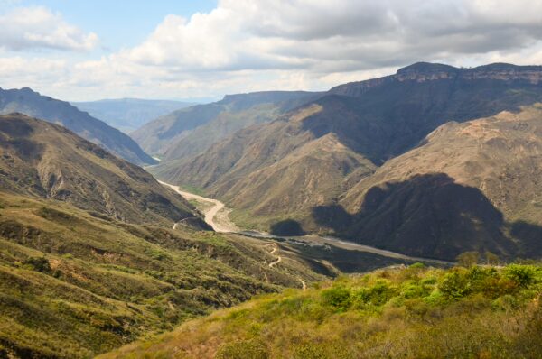 Breathtaking view of Chicamocha Canyon, showcasing dramatic mountains and a winding river under a blue sky with scattered clouds.