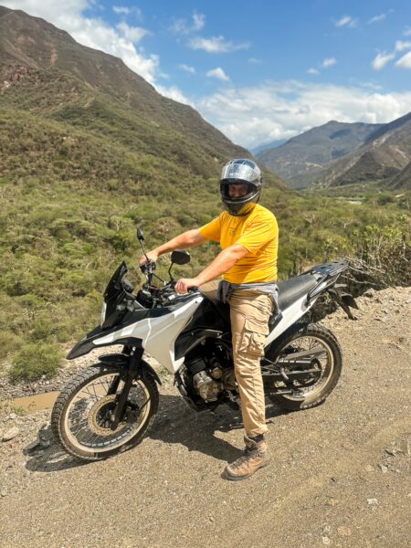 A motorcyclist in a yellow shirt poses on a rugged bike overlooking the stunning landscape of Chicamocha Canyon in Santander, Colombia.