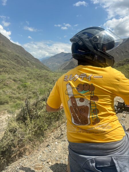 A person in a yellow shirt with a graphic design enjoys a scenic view of Chicamocha Canyon’s lush greenery and mountains.