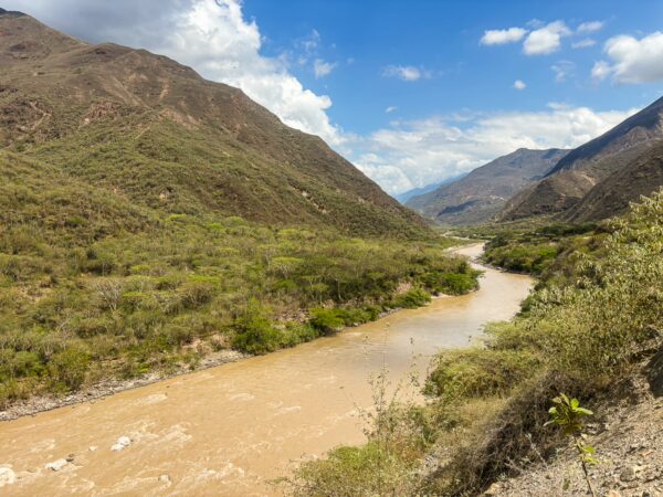 Chicamocha Canyon showcases a winding river flanked by rugged hills and lush green valleys under a bright blue sky.