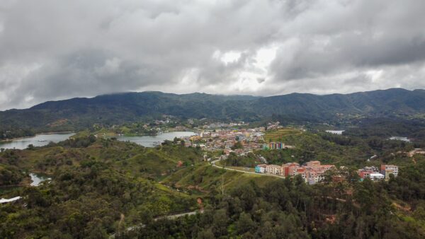El Peñol, Guatape, Antioquia showcases lush green hills and a sprawling town nestled by a vibrant blue lake under cloudy skies.