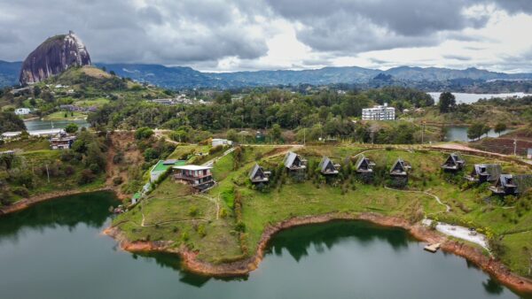 El Peñol Rock in Guatapé, Antioquia, Colombia towers over lush green hills and a serene lake, with modern cabins on the shore.