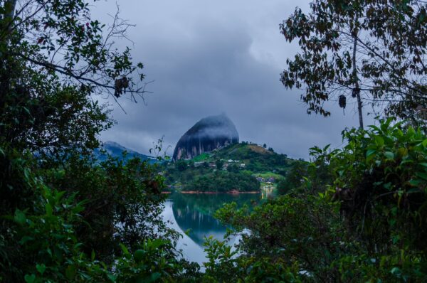El Peñol Rock in Guatapé, Antioquia, Colombia, rises dramatically amidst lush greenery and a serene lake, under a cloudy sky.