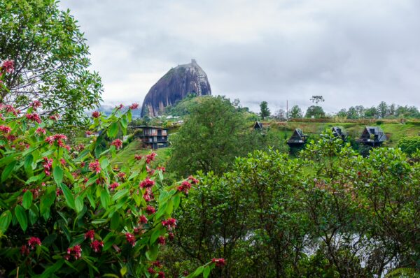 El Peñol Rock in Guatapé, Antioquia, Colombia, rises majestically amidst lush greenery and vibrant flowers under a cloudy sky.
