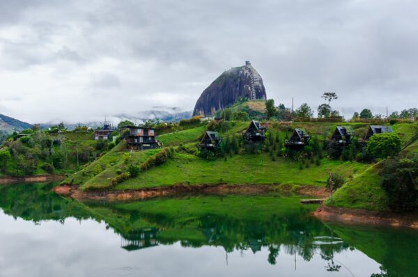El Peñol Rock in Guatapé, Antioquia, Colombia, rises dramatically above a calm lake, surrounded by green hills and quaint cabins.