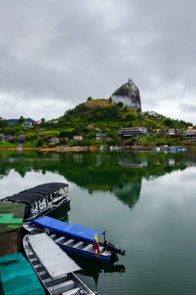 El Peñol rock rises above a tranquil lake in Guatapé, Antioquia, Colombia, surrounded by colorful boats and lush greenery.