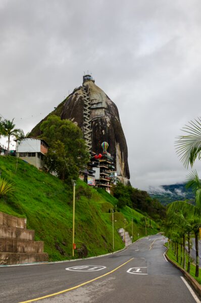 El Peñol Rock in Guatapé, Antioquia, Colombia, towers above lush greenery and a winding road leading to its base.